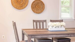 Una zona de comedor con una mesa de madera, dos individuales tejidos y un jarrón con flores blancas.
