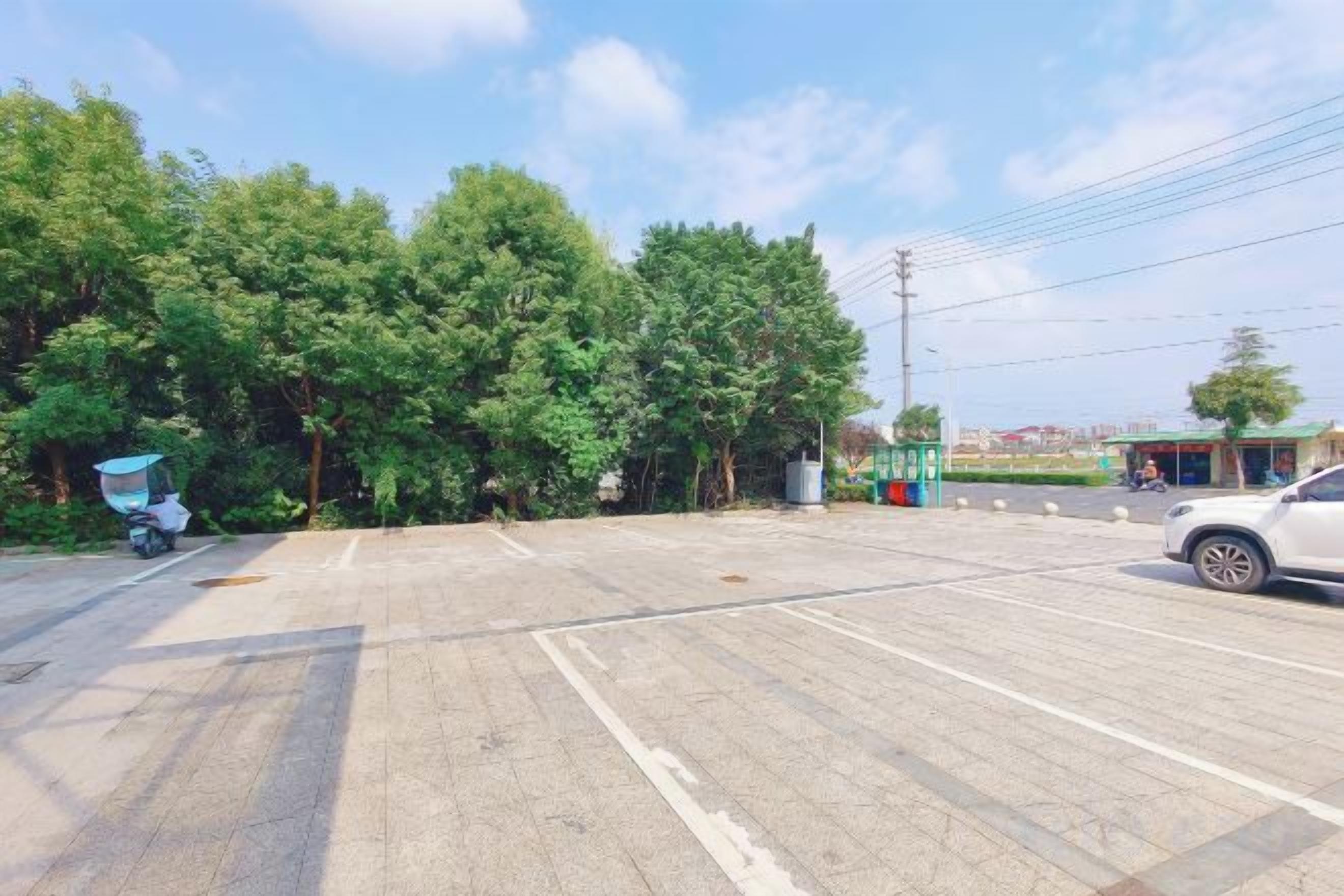 An empty parking lot with trees and a building in the background.