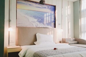 Ein Hotelzimmer mit Bett, Nachttischen, einer Wandlampe und einem großen Gemälde mit Strandmotiv.