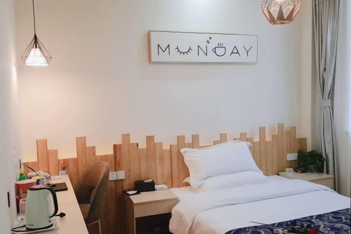 Een hotelkamer met een bed, een bureau met waterkoker, een stoel, een houten hoofdbord en een bord aan de muur.
