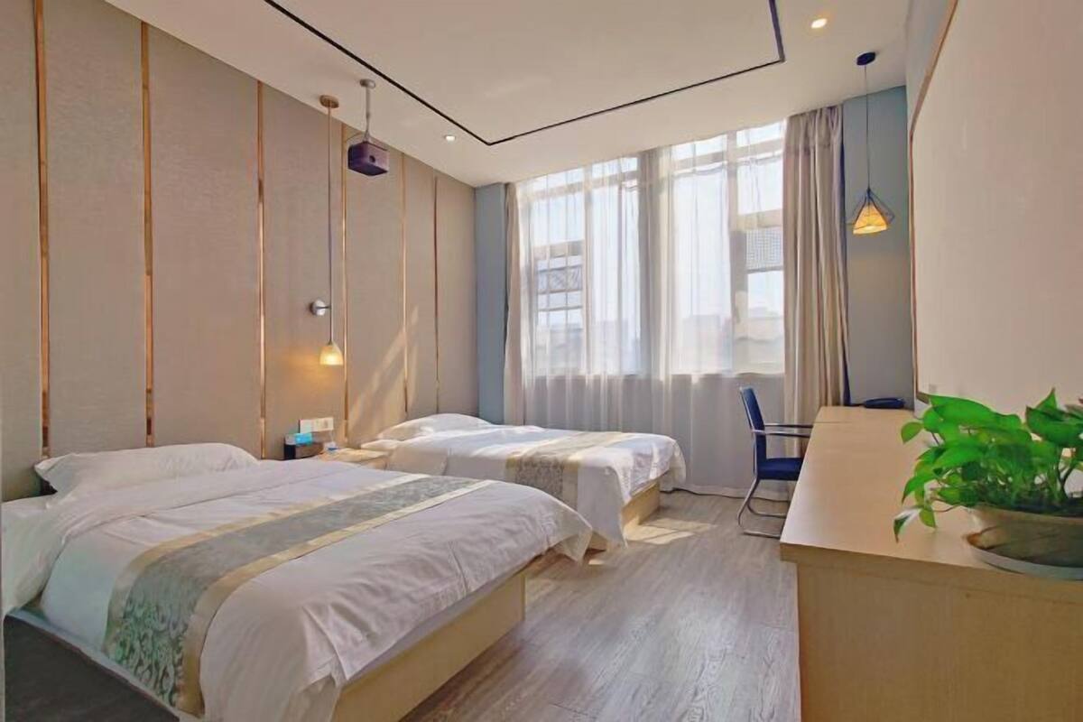 Een hotelkamer met twee bedden, een bureau, een stoel en een potplant.