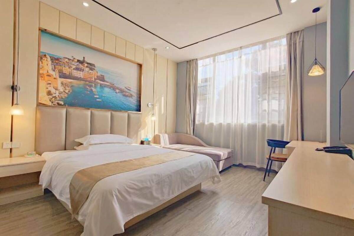 Een hotelkamer met een bed, een bureau en een schilderij van een kustplaats.