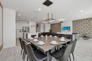 Un espace de salle à manger moderne, avec une grande table dressée pour six personnes, entourée de chaises, dans une pièce bien éclairée avec un mur en pierre et un tableau.