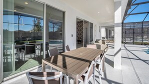 An outdoor dining area with a wooden table and chairs, large glass doors, and a view of a swimming pool. - Beautiful 9Bed Home Close to Disney-2613CA (Kissimmee)