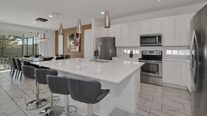 A modern kitchen with white cabinetry, stainless steel appliances, and a central island with bar stools. - Beautiful 9Bed Home Close to Disney-2613CA (Kissimmee)