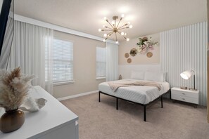 A bedroom with a bed, bedside table, lamp, decorative wall, and curtains.