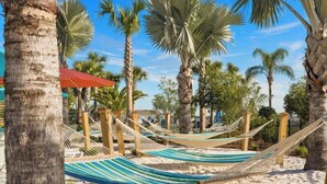 Escena de playa con hamacas, palmeras y una zona arenosa.