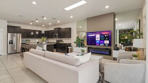 Una cocina moderna con armarios oscuros, un refrigerador de acero inoxidable y un televisor de pantalla plana mostrando servicios de transmisión.