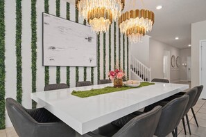 A modern dining area with a white table, black chairs, a chandelier, and a staircase in the background.