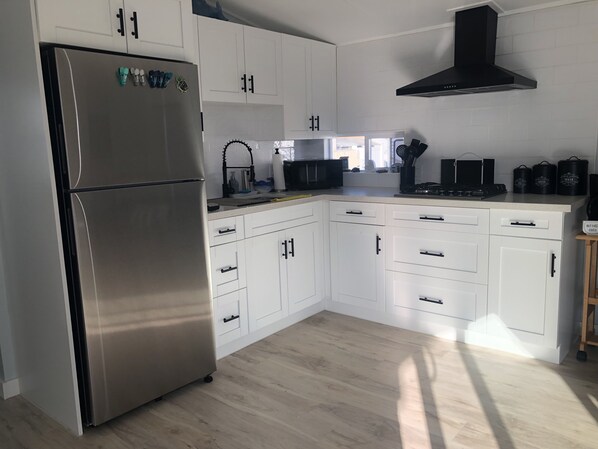 A modern kitchen with white cabinets, a stainless steel refrigerator, a black range hood, and a wooden floor. - Tropical Tiny Home Getaway in Key Largo (Key Largo)