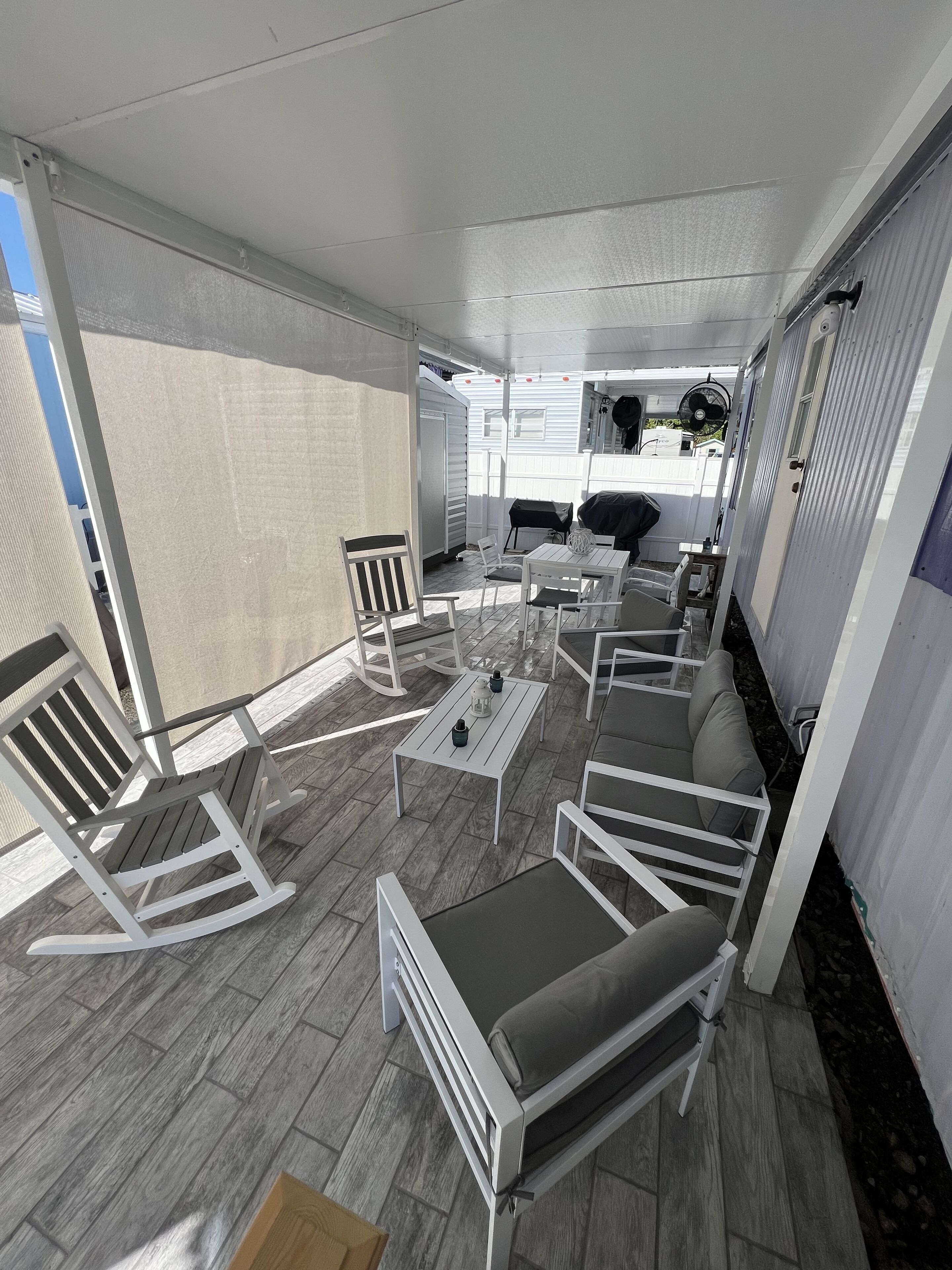Een overdekt terras met witte meubels, waaronder stoelen en een bank, en een tafel met decoratieve objecten.