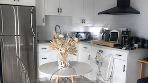 A modern kitchen with white cabinets, a stainless steel refrigerator, a microwave, and a black range hood. There is a round table with clear chairs and a vase with dried flowers. - Tropical Getaway in the heart of Key Largo (Key Largo)
