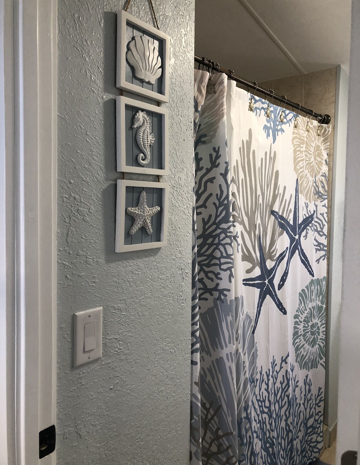 A bathroom with a textured wall, a shower curtain with a coral reef pattern, and three framed sea creature decorations.
