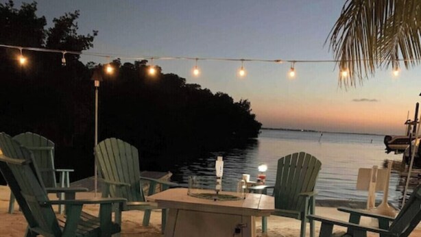 A beachside seating area with Adirondack chairs and a table, string lights overhead, and a view of the water at dusk. - Tropical Getaway in the heart of Key Largo (Key Largo)