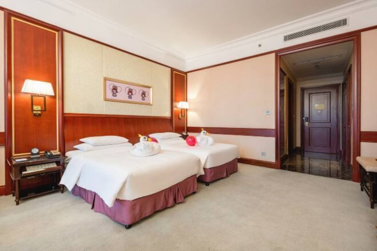 Habitación de hotel con dos camas, una mesita de noche con lámpara, un reloj y un cuadro en la pared.