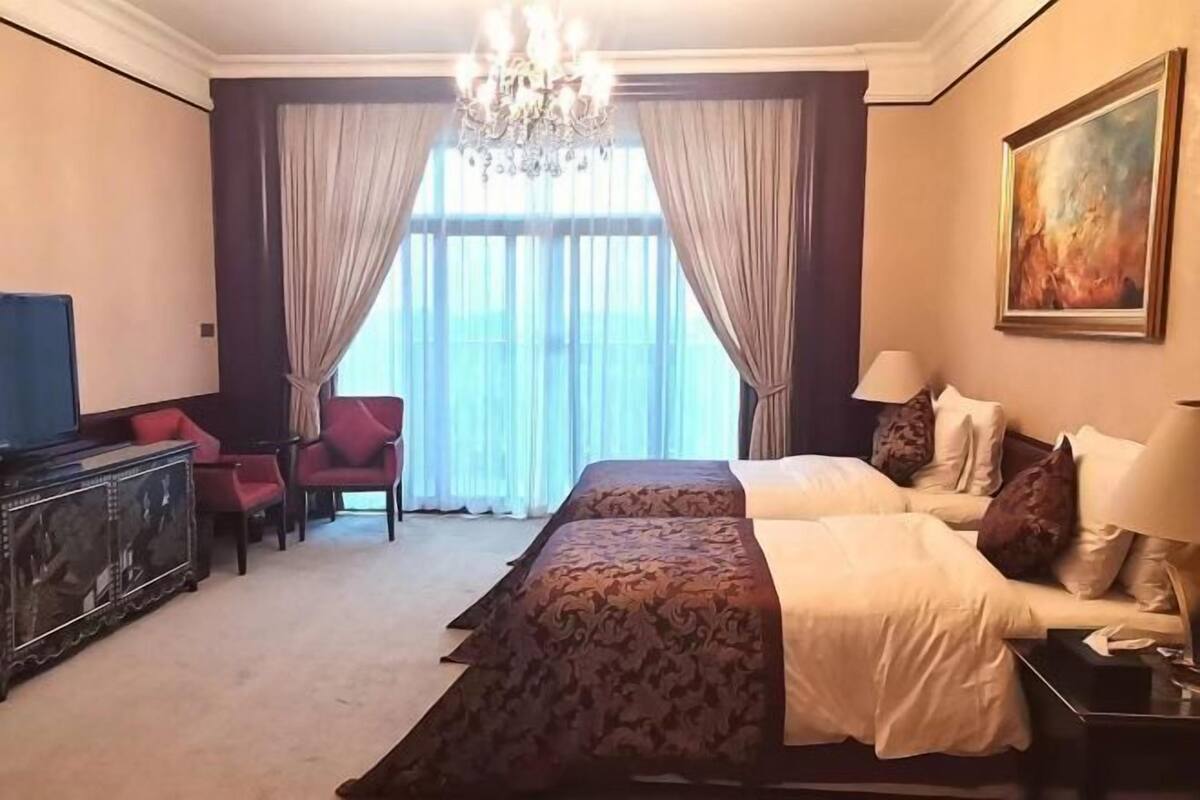 A hotel room with two beds, a chandelier, a painting, and a TV.