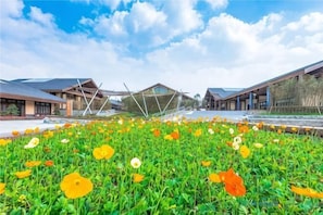 A courtyard with a flower garden, modern buildings, and a clear sky. - Hengda Hotel (Meishan)