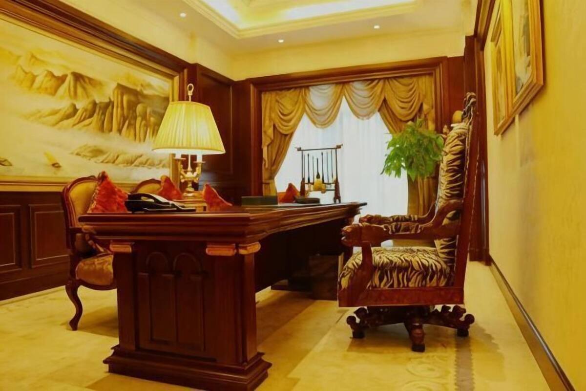 A room with a desk, chairs, a lamp, a plant, and a painting on the wall.