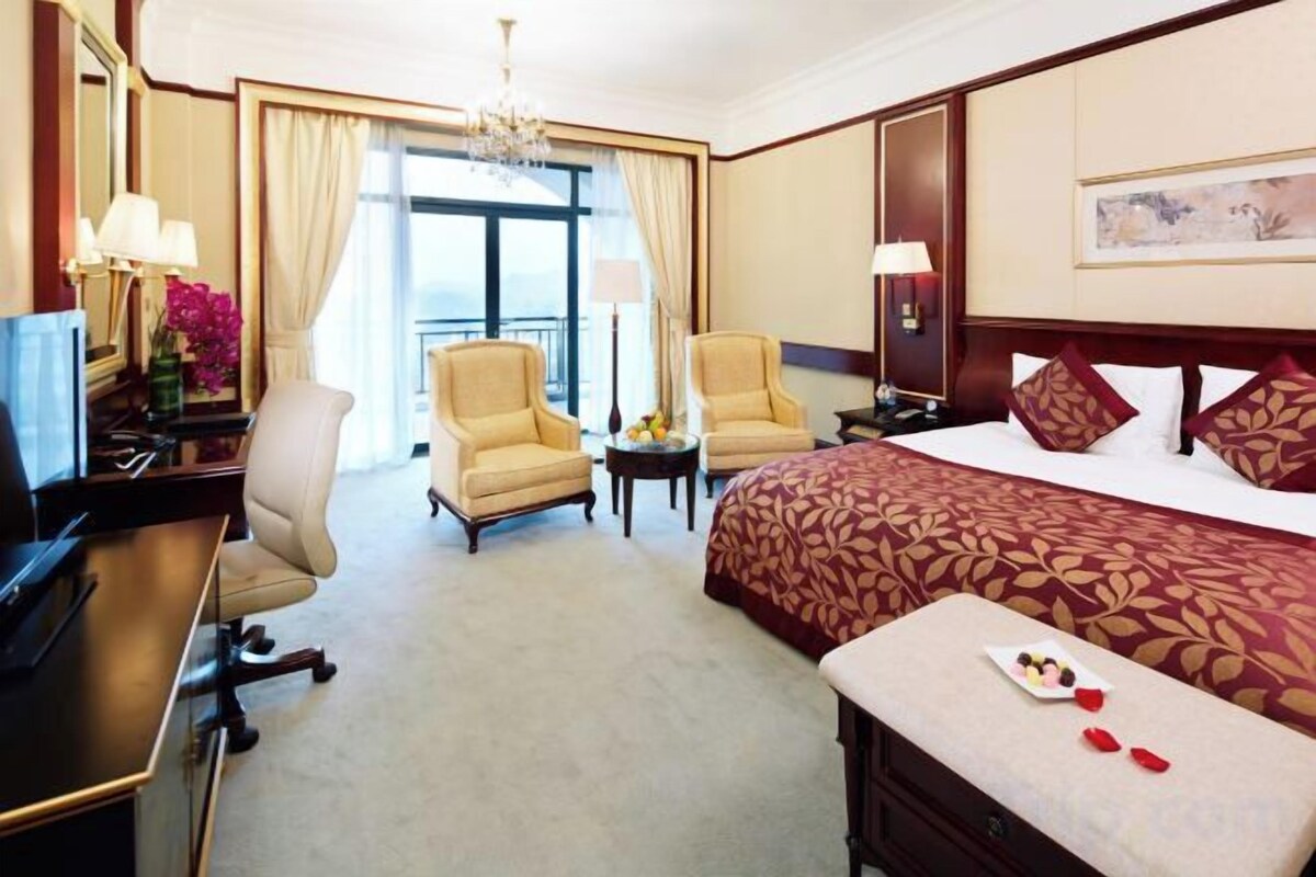 Habitación de hotel con cama, dos sillones, un escritorio, televisión y vistas al exterior.