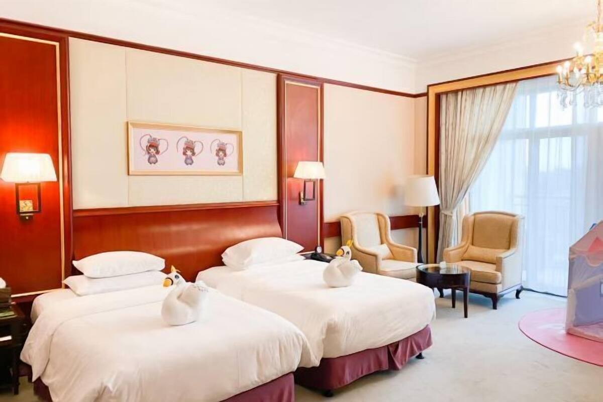 A hotel room with two beds, a chandelier, a desk, and a chair.