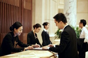 A reception desk in a hotel lobby with a marble floor and a wooden panel wall. - Hengda Hotel (Meishan)