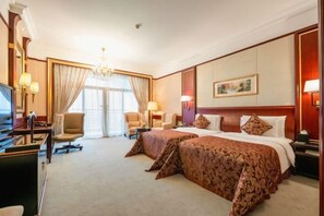 Habitación de hotel con dos camas, un escritorio, una silla, un televisor y un candelabro.