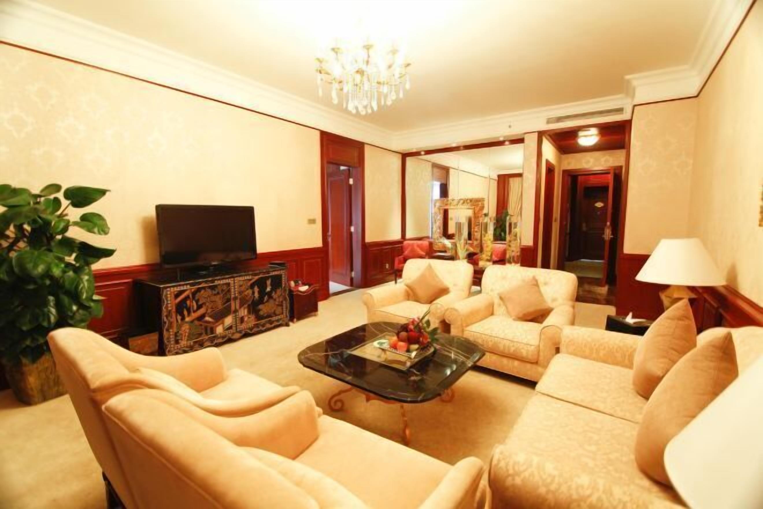 A spacious living room with beige sofas, a glass coffee table, a television, and a large mirror.