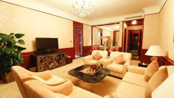A spacious living room with beige sofas, a glass coffee table, a television, and a large mirror.