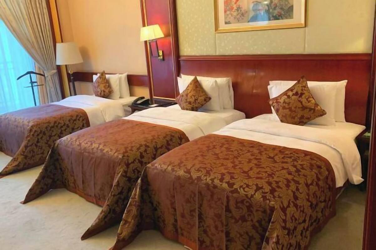 A hotel room with two beds, each with a patterned bedspread and pillows, a bedside lamp, and a painting on the wall.