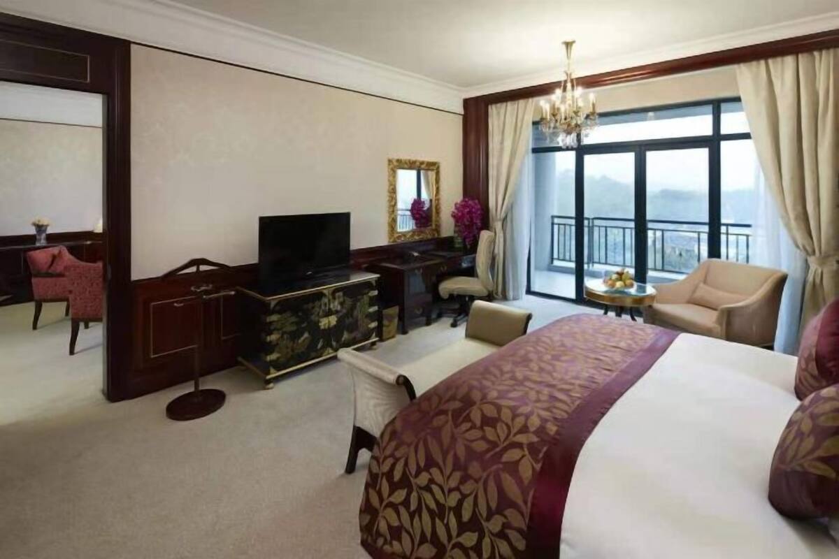 Habitación de hotel con una cama grande, un escritorio con televisor, una silla, una mesita y vistas al exterior.