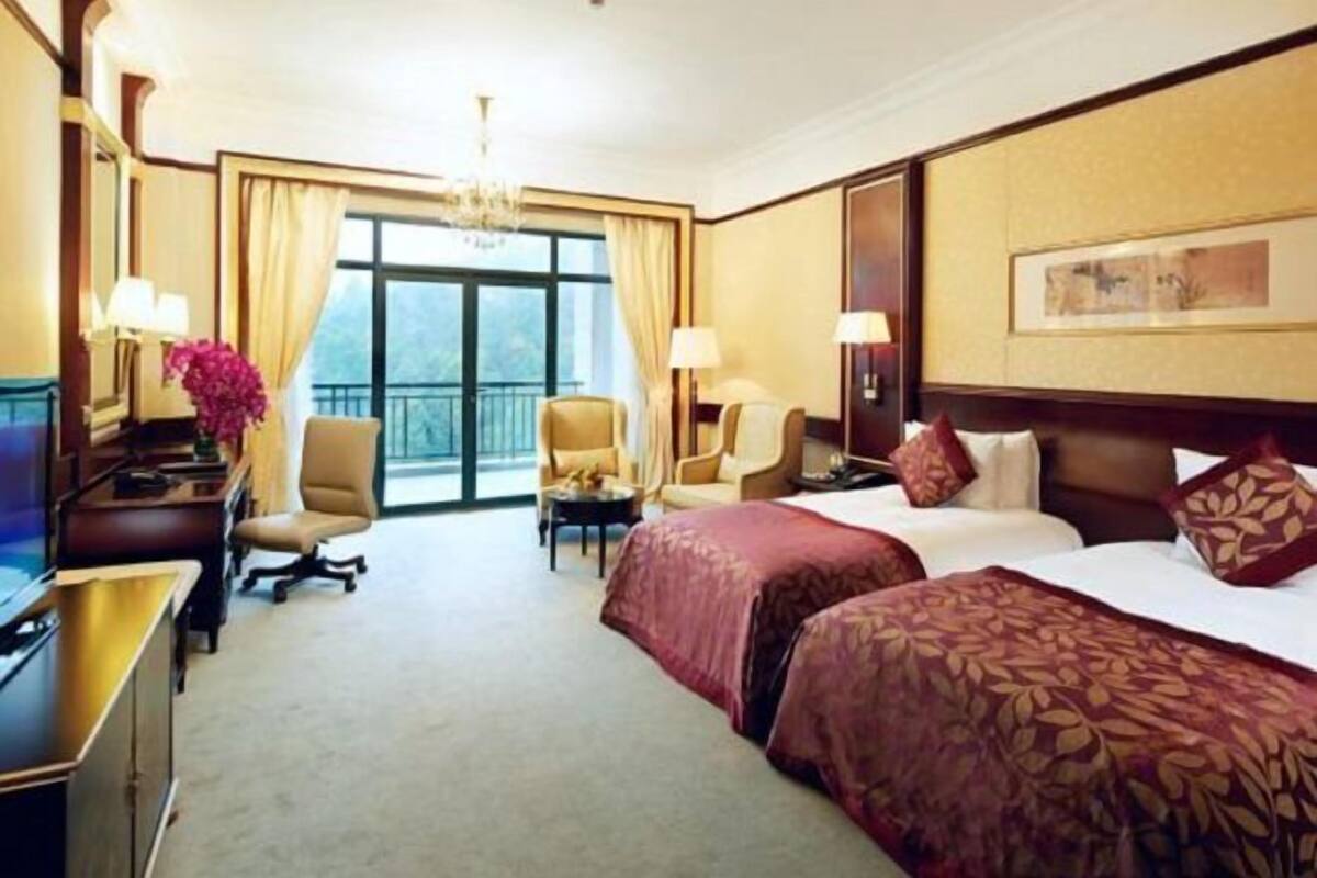 A hotel room with two beds, a desk, a chair, a TV, and a large window with curtains.