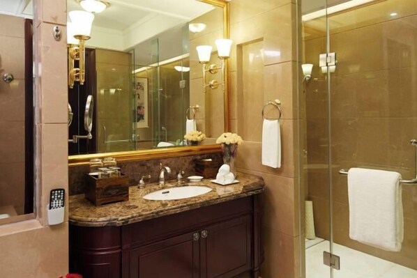 Un baño con tocador de mármol, un espejo grande, cerramiento de ducha de vidrio y un perchero para toallas.