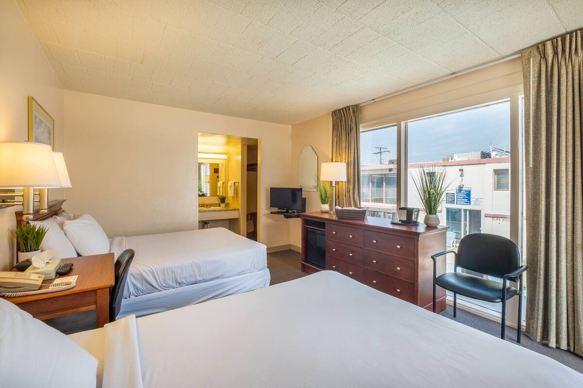 A hotel room with two beds, a desk with a lamp, a dresser, a chair, and a TV.