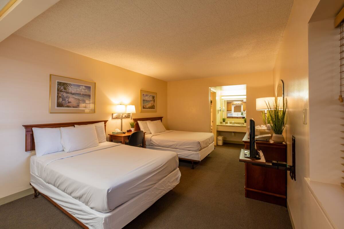 A hotel room with two beds, a desk with a computer, a mirror, and a window.