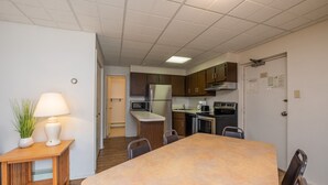 A compact kitchen with a central island, a dining table, and a small side table with a lamp and plant. - Tahiti Inn  (Ocean City)