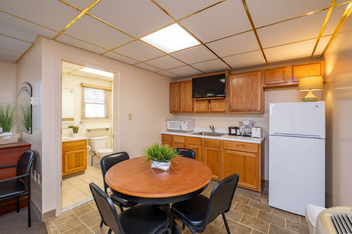 A compact kitchen with wooden cabinets, a microwave, a refrigerator, and a dining area with a table and chairs.