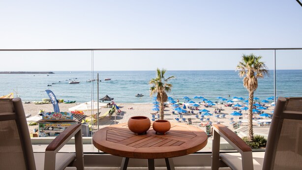 Un balcón con vista a la playa, dos macetas de terracota y una mesa.