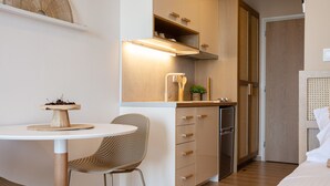 Cocina compacta con zona de comedor, que incluye una mesa redonda, sillas de mimbre y un horno empotrado.
