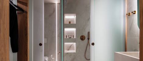 A modern bathroom with a glass shower enclosure, marble walls, and built-in shelves.
