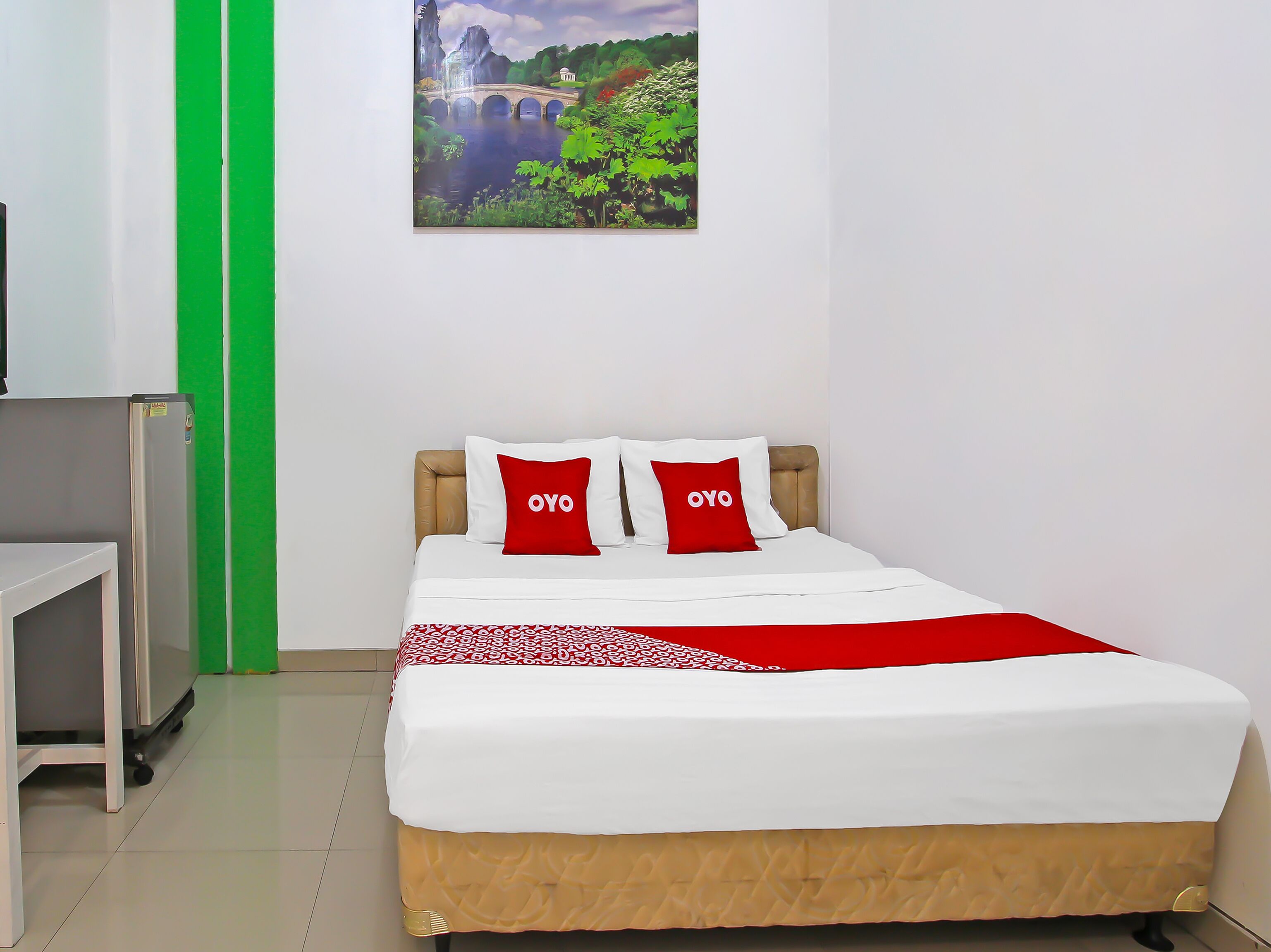 A neatly made bed with a white and red bedspread, two red pillows with "OYO" on them, and a green door to the left.