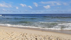 Ein sandiger Strand mit Wellen und blauem Himmel.