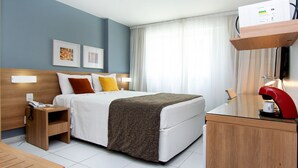 Ein Hotelzimmer mit einem Bett, Nachttisch, Lampe und Schreibtisch mit Kaffeemaschine.