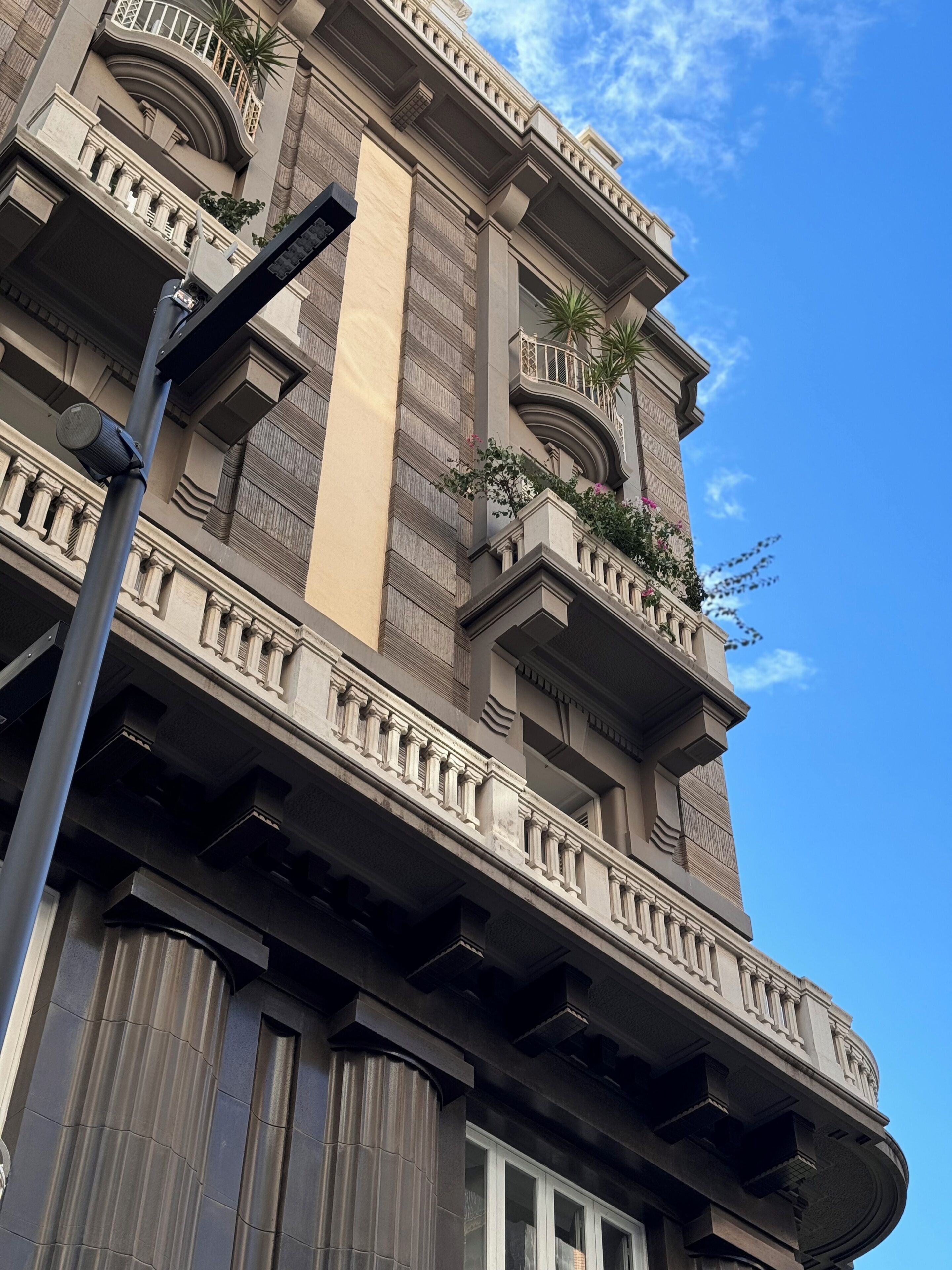 A multi-story building with balconies, columns, and a clear sky.