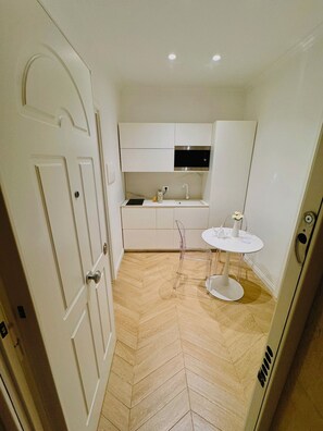Een compacte keuken met een visgraatvloer, een witte spoelbak en een kleine ronde tafel met een vaas.