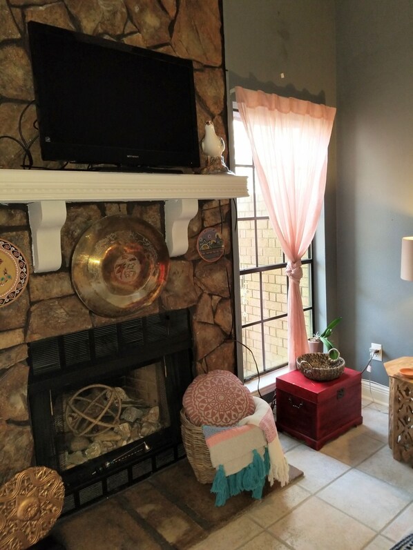 A stone fireplace with a flat-screen TV above it, a decorative bowl, and a basket with a blanket.