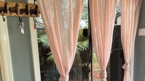 A room with a glass door, pink curtains tied back, a woven basket on a wooden stool, and a patterned rug on the floor.
