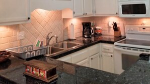 A kitchen with white cabinets, a black countertop, a white stove, and a microwave.