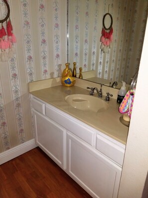 A bathroom with a beige sink, white cabinets, floral wallpaper, and a mirror.