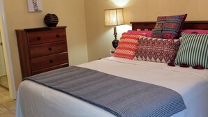 A bedroom with a large bed, a wooden dresser, a chandelier, a wall-mounted lamp, and decorative pillows.