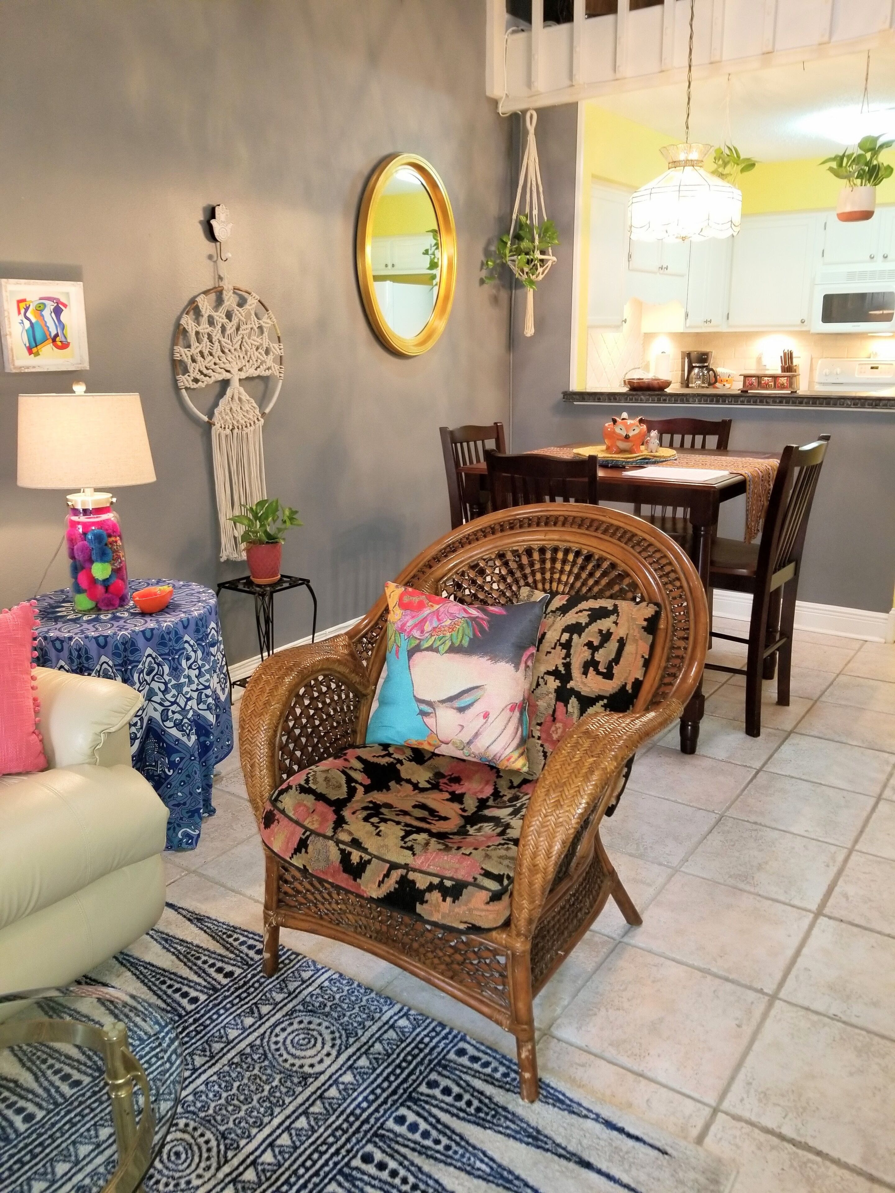 Un coin repas avec une chaise en osier, une table recouverte d’une nappe à motifs et une décoration murale en macramé.